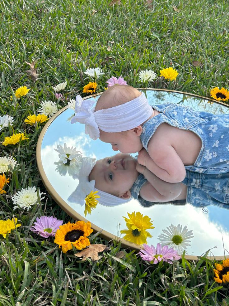 flowers are around baby which sitting on mirror 
